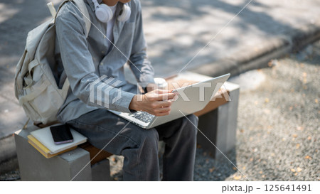 Close up of an asian man touching or adjusting his laptop screen, sitting on the sidewalk bench. Close up of an asian man touching or adjusting his laptop screen, sitting on the sidewalk bench. 125641491