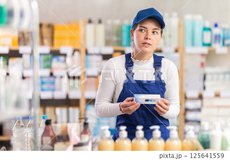In sales area of pharmacy, builder woman examines packaging of gel for burns In sales area of pharmacy, builder woman examines packaging of gel for burns 125641559