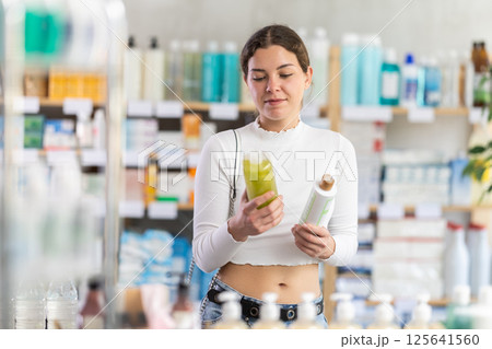 Female shopper in summer clothes chooses medicated shampoo at pharmacy Female shopper in summer clothes chooses medicated shampoo at pharmacy 125641560