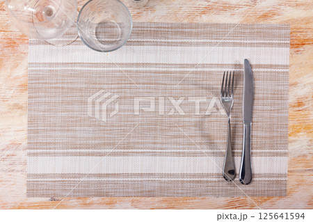 Cloth napkin with cutlery, cutlery complemented by transparent glasses for drinks and salt shaker. Cloth napkin with cutlery, cutlery complemented by transparent glasses for drinks and salt shaker. 125641594