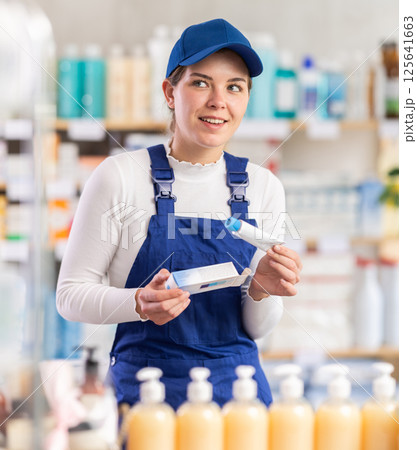 In sales area of pharmacy, builder woman examines packaging of gel for burns 125641663