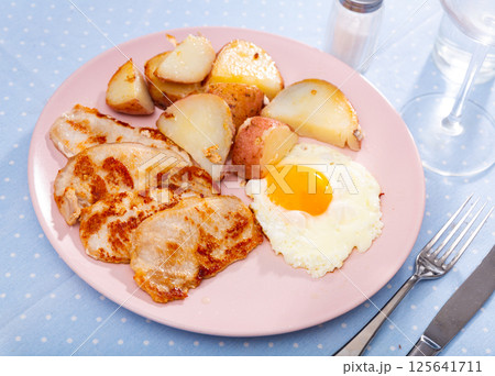 Fried pork fillet with scrambled eggs and french fries closeup Fried pork fillet with scrambled eggs and french fries closeup 125641711