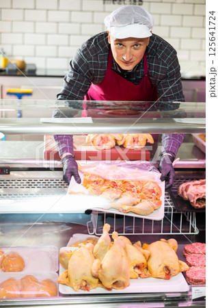 Adult man puts chicken meat in showcase 125641724