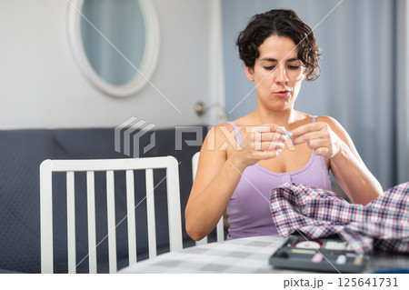 Woman sewing button on shirt sleeve at home Woman sewing button on shirt sleeve at home 125641731