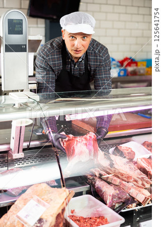 Adult man puts beef ribs in showcase Adult man puts beef ribs in showcase 125641754