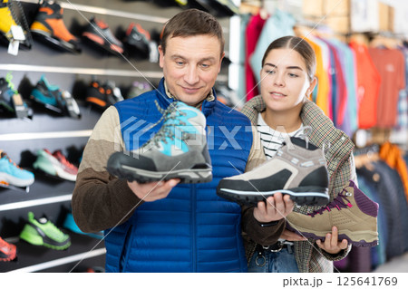 Man and young girl chooses winter sport shoes together for an hiking trip in sports store Man and young girl chooses winter sport shoes together for an hiking trip in sports store 125641769