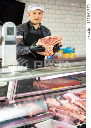 Confident male butcher showing a big piece of beef ribs in butchery 125641770