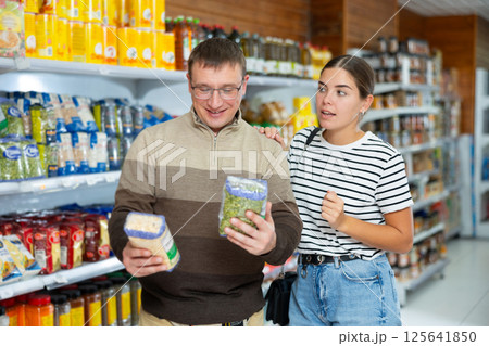 Girl helps man choose package of pea cereals in supermarket department 125641850