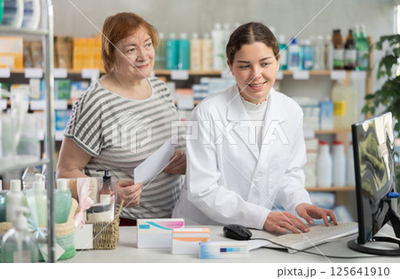 Woman pharmacist looking for prescription on computer for buyer Woman pharmacist looking for prescription on computer for buyer 125641910