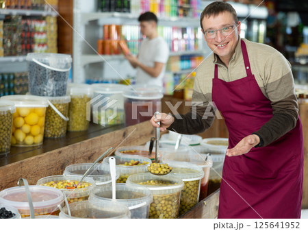 Frienfly male supermarket grocery seller offers to buy pickled green olives 125641952