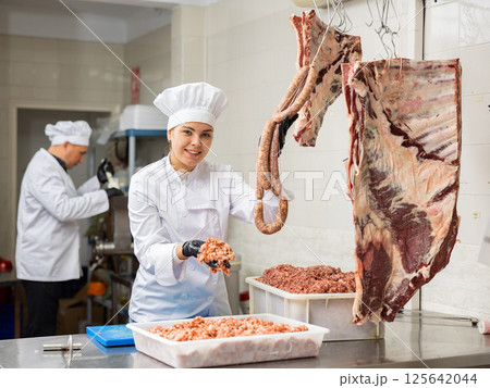 Happy female butcher showing sausages made of minced beef meat in butcher shop 125642044