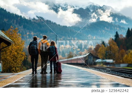 Three Young Travelers at a Mountainous Train Station Platform on a Rainy Day with Autumn Colors and Dramatic Cloudy Skies in the Background Three Young Travelers at a Mountainous Train Station Platform on a Rainy Day with Autumn Colors and Dramatic Cloudy Skies in the Background 125642242