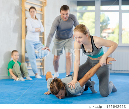 At self-defense training, trainer teaches teenage girl technique of grabbing arm and lowering opponent to floor At self-defense training, trainer teaches teenage girl technique of grabbing arm and lowering opponent to floor 125642428