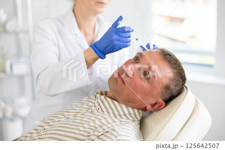 Man applying rejuvenating treatments by female doctor. Man applying rejuvenating treatments by female doctor. 125642507