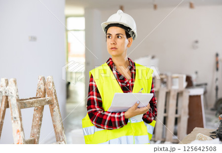 Focused young female civil engineer making notes at construction site indoors Focused young female civil engineer making notes at construction site indoors 125642508