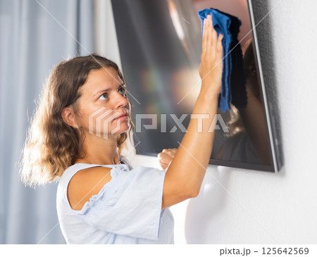 Housewife wipes dust from the TV at home with rag 125642569