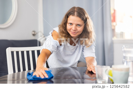 Positive brunette woman cleaning table at home 125642582