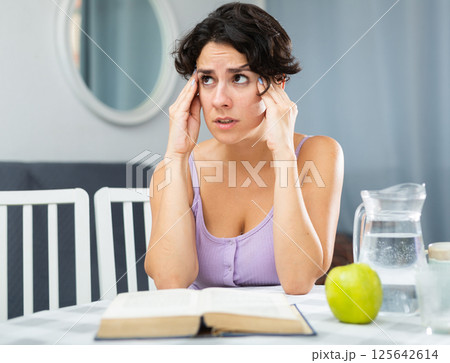 Woman with a headache trying to learn lessons for university exams 125642614