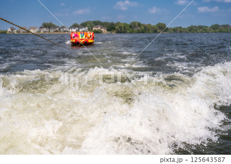 Inflatable raft being pulled at a high speed by a boat in a recreational activity called tubing Inflatable raft being pulled at a high speed by a boat in a recreational activity called tubing 125643587
