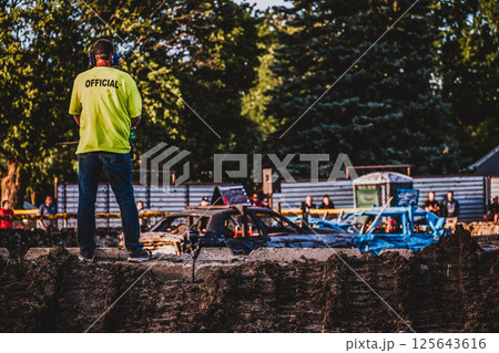 Official standing on a dirt embankment overlooking a demolition derby.  125643616