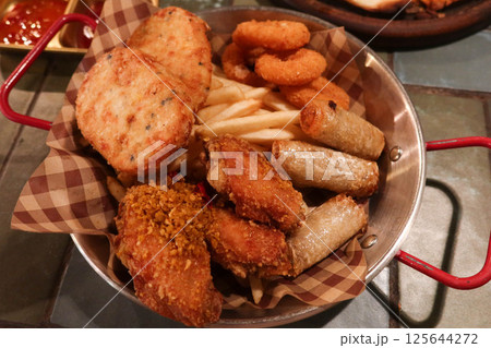 close up of assorted Thai appetiser including stir fried fishcake, round patties, french fries, onion rings, spring rolls, and chicken wings in a metal basket with sweet and sour sauce  125644272