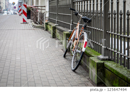 Abandoned Bicycle Leaning Against Fence on Paved Sidewalk Abandoned Bicycle Leaning Against Fence on Paved Sidewalk 125647494