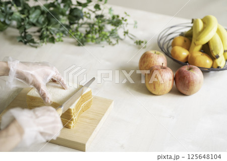 サンドイッチを切る女性、フルーツと植物のあるキッチン サンドイッチを切る女性、フルーツと植物のあるキッチン 125648104