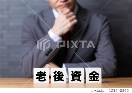 老後資金のブロックとスーツを着て悩むミドル男性ビジネスマン 老後資金のブロックとスーツを着て悩むミドル男性ビジネスマン 125648846