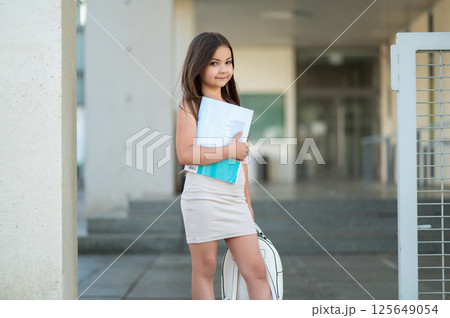 Little child with brown hair in skirt standing in street on her way to school carrying backpack Little child with brown hair in skirt standing in street on her way to school carrying backpack 125649054