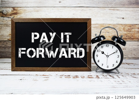 Pay It Forward text message and alarm clock on wooden background Pay It Forward text message and alarm clock on wooden background 125649903