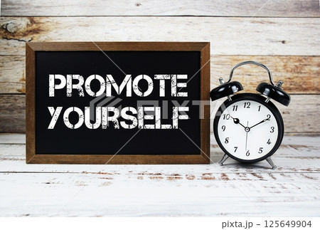 Promote Yourself text message and alarm clock on wooden background Promote Yourself text message and alarm clock on wooden background 125649904