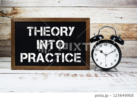 Theory Into Practice text message and alarm clock on wooden background 125649908