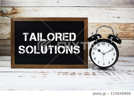 Tailored Solutions text message and alarm clock on wooden background Tailored Solutions text message and alarm clock on wooden background 125649909