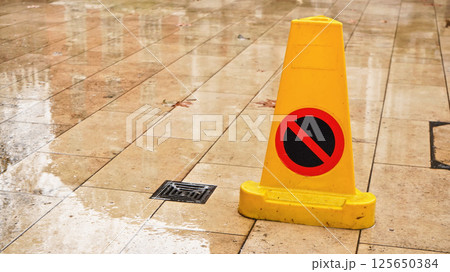 Yellow plastic cone with warning sign on slippery wet tile floor 125650384