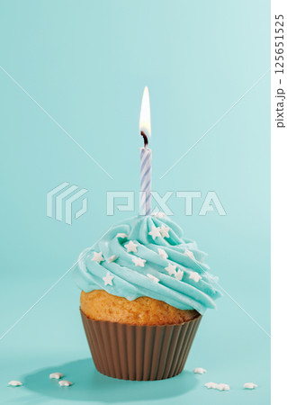 Festive cupcake topped with swirled frosting and a lit candle 125651525