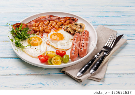 A classic breakfast plate featuring sunny-side-up eggs, crispy bacon, sausages, and fresh tomatoes 125651637