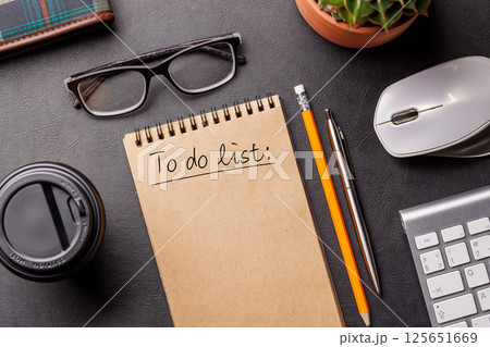 Organized work desk setup with PC, office supplies, coffee, and a notepad for writing a to-do list 125651669