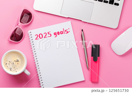Modern pink desk with laptop, coffee, stationery, and a notepad titled 2025 Goals Modern pink desk with laptop, coffee, stationery, and a notepad titled 2025 Goals 125651730