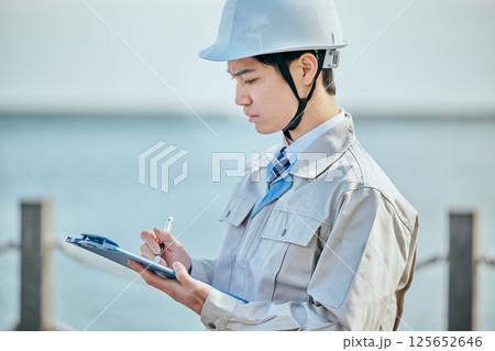 メモを取る作業着姿の20代の若い男性 メモを取る作業着姿の20代の若い男性 125652646