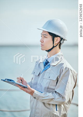 メモを取る作業着姿の20代の若い男性 メモを取る作業着姿の20代の若い男性 125652648