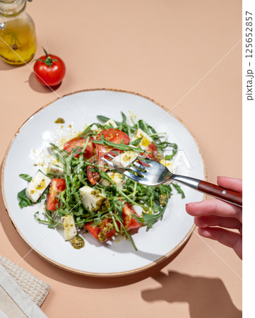 Hand holding fork fresh arugula salad with cherry tomatoes, mozzarella, pesto sauce 125652857
