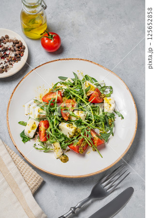 Arugula salad with cherry tomatoes, mozzarella and pesto sauce on a light background 125652858