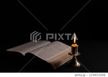 Dark, an antique candle cast its light on the old Bible, its flames flickering gently over the book on the table, symbolizing the enduring essence of religion. candle, bible, dark, light, book, old. Dark, an antique candle cast its light on the old Bible, its flames flickering gently over the book on the table, symbolizing the enduring essence of religion. candle, bible, dark, light, book, old. 125653208
