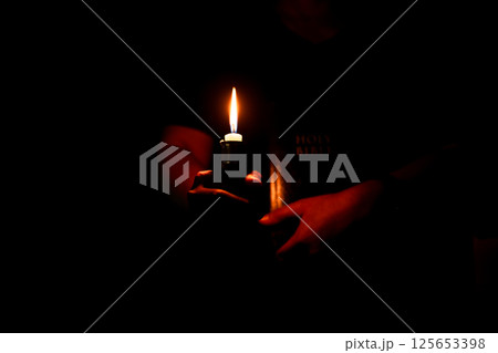 In the church, candle flickered beside cross as Christians gathered to pray, their faith in Jesus and spiritual devotion illuminated by Bible in background, deepening their Catholic worship. In the church, candle flickered beside cross as Christians gathered to pray, their faith in Jesus and spiritual devotion illuminated by Bible in background, deepening their Catholic worship. 125653398