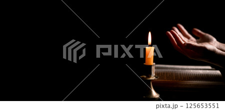 In the dark, hand clasped in prayer, illuminated by the soft candlelight, as black flames of candle fire flickered gently. candle, pray, hand, prayer, black, fire, flames, candlelight, light, dark. In the dark, hand clasped in prayer, illuminated by the soft candlelight, as black flames of candle fire flickered gently. candle, pray, hand, prayer, black, fire, flames, candlelight, light, dark. 125653551