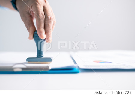 Notary placed their stamp of approval on the document as the lawyer and business person finalized the contract, ensuring all legal paperwork was in order. stamp, approval, document, contract, person. 125653723