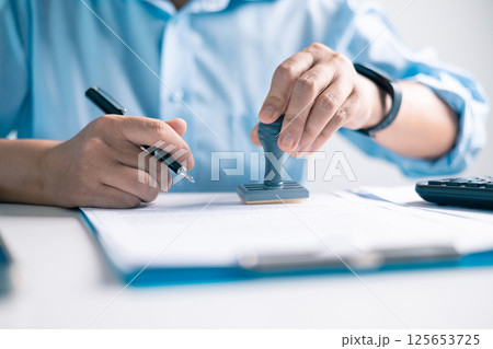 Notary placed their stamp of approval on the document as the lawyer and business person finalized the contract, ensuring all legal paperwork was in order. stamp, approval, document, contract, person. Notary placed their stamp of approval on the document as the lawyer and business person finalized the contract, ensuring all legal paperwork was in order. stamp, approval, document, contract, person. 125653725