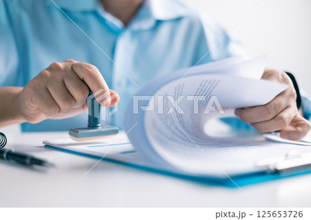 Notary placed their stamp of approval on the document as the lawyer and business person finalized the contract, ensuring all legal paperwork was in order. stamp, approval, document, contract, person. 125653726