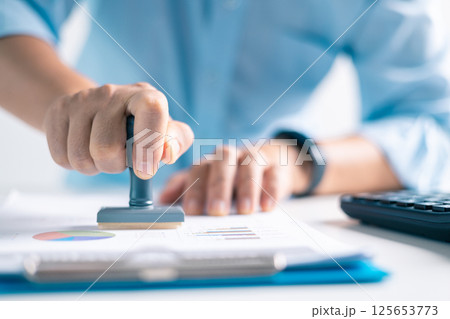 Notary placed their stamp of approval on the document as the lawyer and business person finalized the contract, ensuring all legal paperwork was in order. stamp, approval, document, contract, person. 125653773