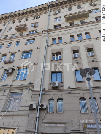 A modest gray building with stacked balconies, uniform windows, and visible air conditioning installations. This photo represents functional urban architecture balancing affordability and space 125654885